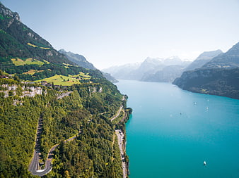 Aerial View of Turquoise Lake Surrounded by Green Mountains and Winding Roads