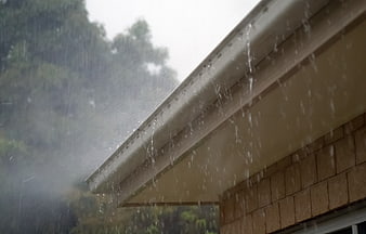 Heavy rain pouring from a house roof gutter during a storm