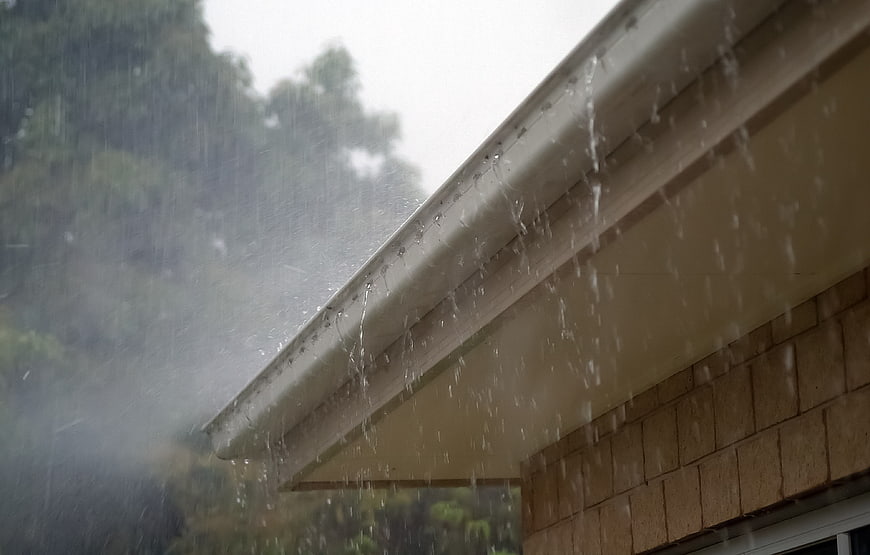 Heavy rain pouring from a house roof gutter during a storm
