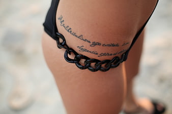 Close-up of woman's hip with tattoo and black chain accessory