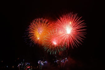 Vibrant red and orange fireworks exploding in night sky