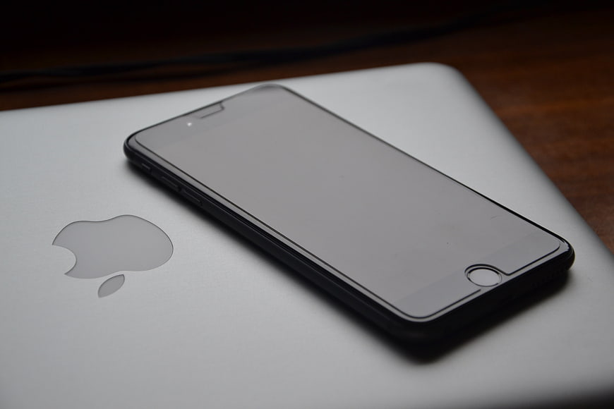 Black smartphone resting on silver laptop with Apple logo