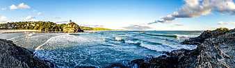 Panoramic coastal landscape featuring turquoise ocean waves and rocky shoreline