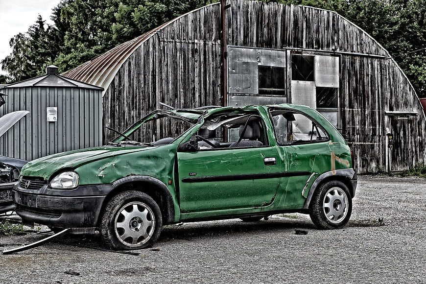 Damaged Green Car in Scrapyard with Barn Background