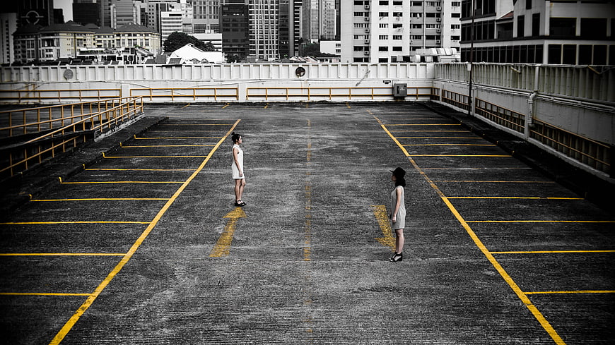 Two women standing in empty parking lot with yellow lines