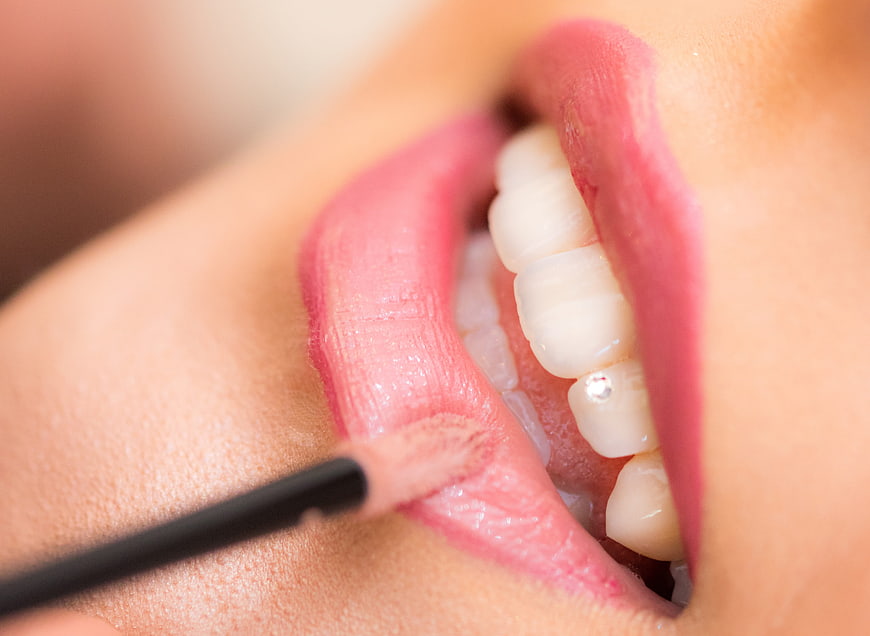 Close-up of woman applying lipstick with tooth gem