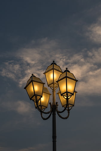Vintage street lanterns glowing against a cloudy evening sky