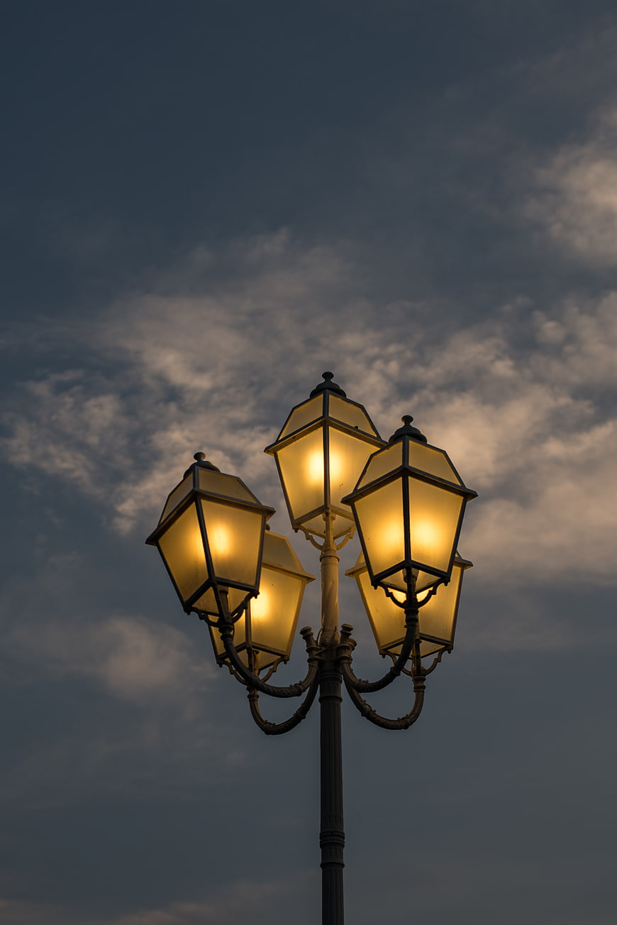 Vintage street lanterns glowing against a cloudy evening sky