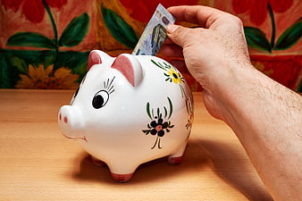 Hand inserting euro banknote into white ceramic piggy bank