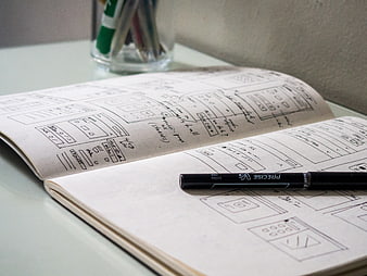 Hand-drawn UI wireframes in a sketchbook with a pen