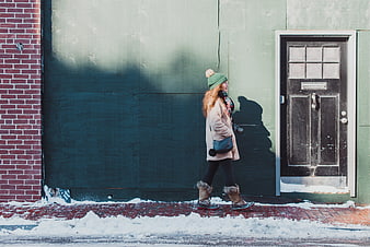 Woman in winter coat walking past green wall in snow