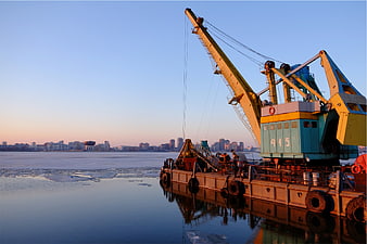 Yellow crane barge on frozen river with city skyline
