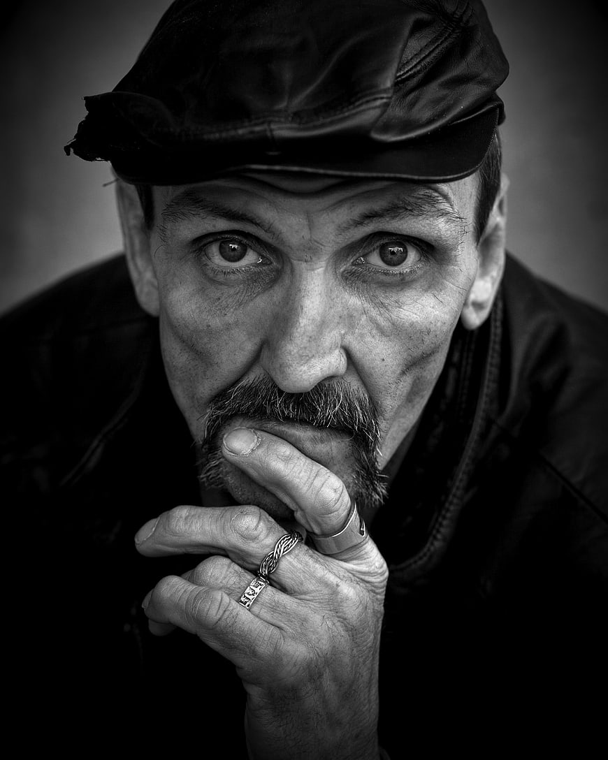 Dramatic black and white portrait of a man with a cap and rings