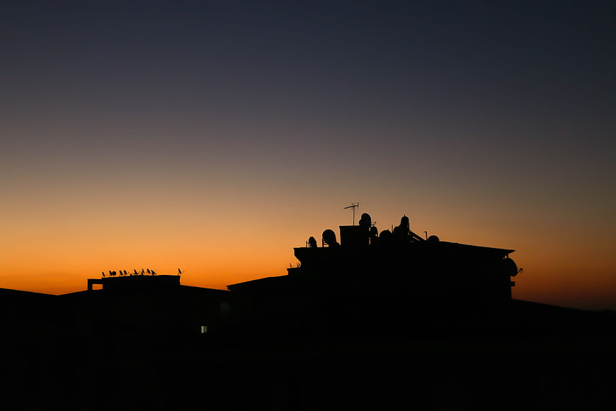 Silhouette of Rooftop with Birds Against Sunset Sky