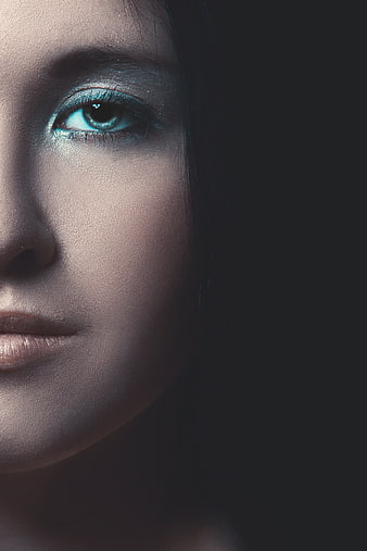 Close-up portrait of woman with blue eye makeup and dark background