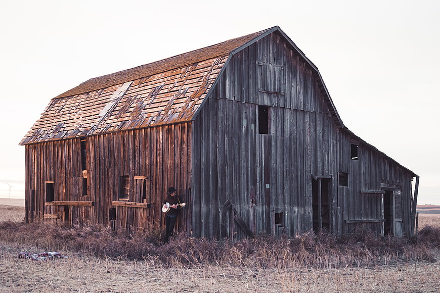 Man playing banjo in front of old abandoned wooden barn