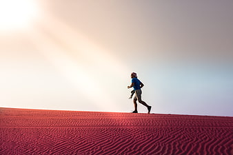 Man running on red sand dune in desert at sunset