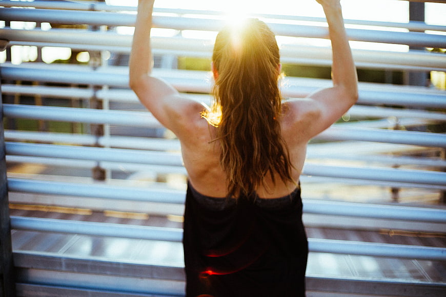 Woman stretching outdoors at sunrise with backlit hair