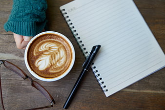 Flat lay of latte art coffee, notebook, and pen on wooden table