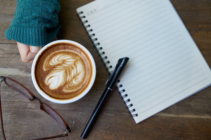 Flat lay of latte art coffee, notebook, and pen on wooden table