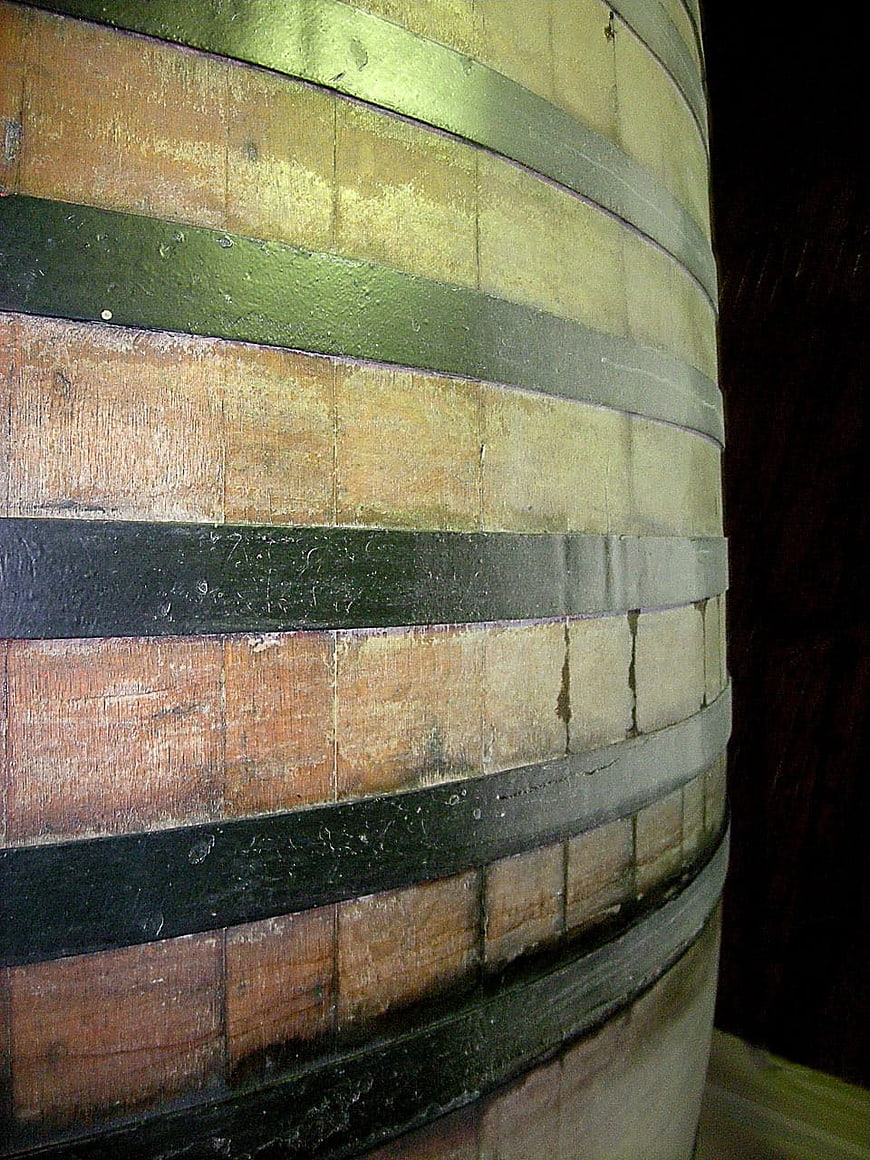 Close-up of weathered wooden barrel with metal hoops in dark cellar