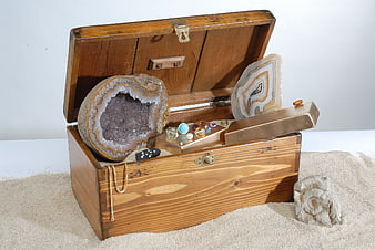 Vintage wooden treasure chest filled with geodes, crystals, and gemstones on sand