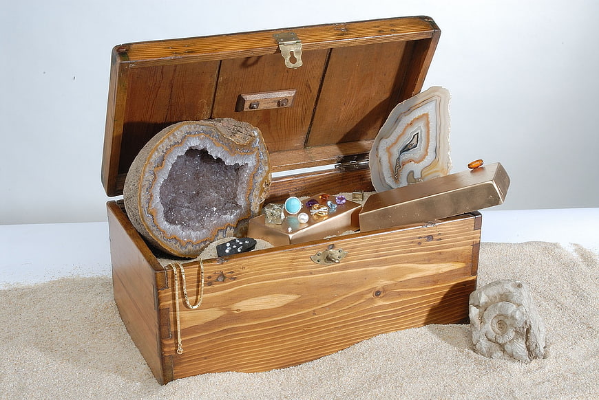 Vintage wooden treasure chest filled with geodes, crystals, and gemstones on sand