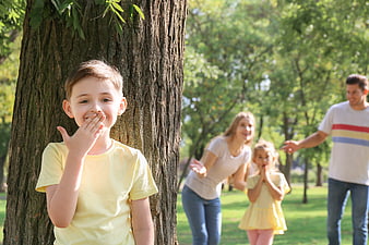 Happy Boy Hiding Behind Tree While Family Plays Hide and Seek