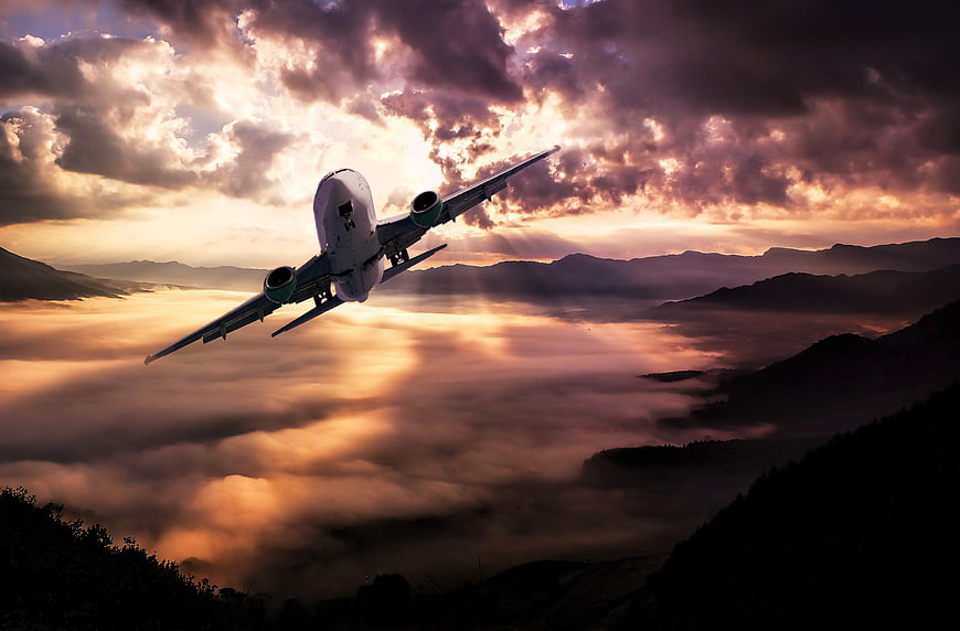 Airplane flying over mountains at sunset with dramatic clouds