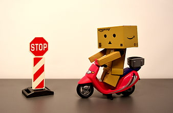 Danbo cardboard figure riding red scooter near stop sign