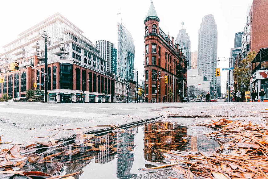Low angle city street with puddle reflection and autumn leaves