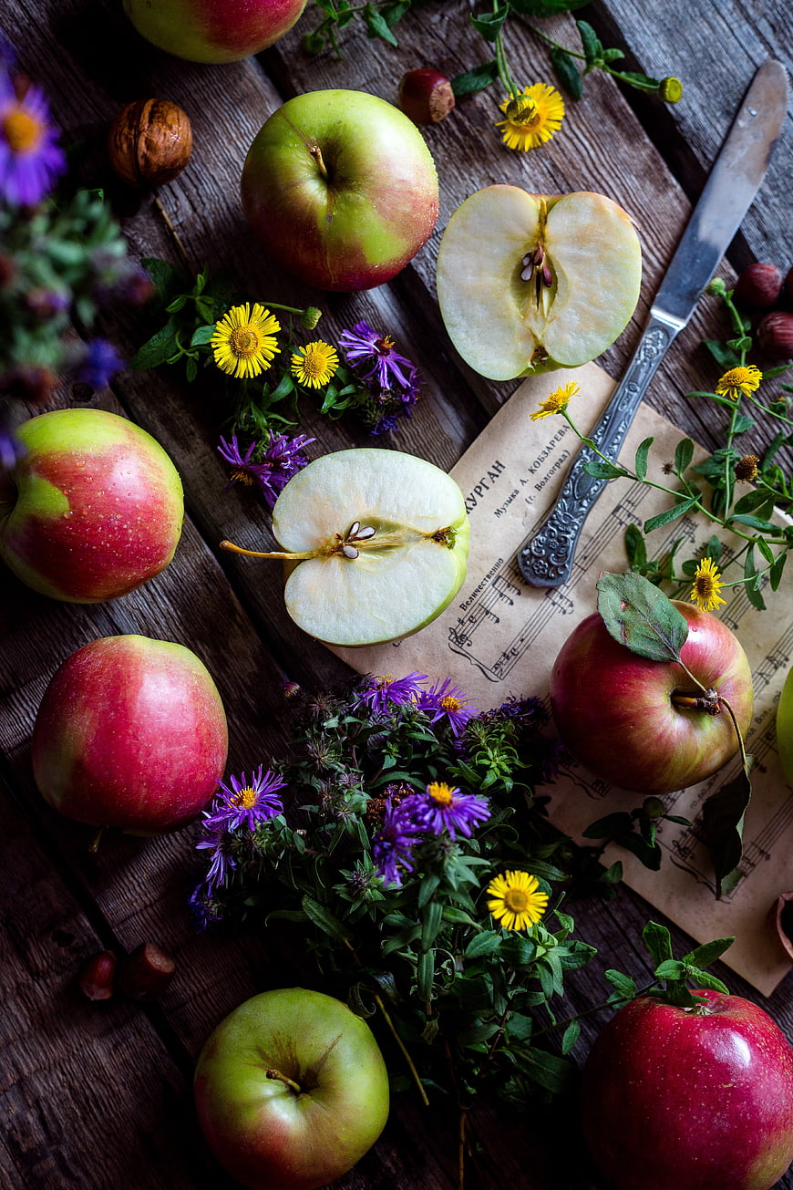 Rustic still life of red apples, flowers, and sheet music on wood