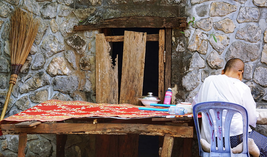 Monk sitting at rustic wooden table against stone wall