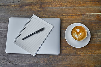 Flat lay of laptop, notebook, pen, and latte art coffee on wooden table
