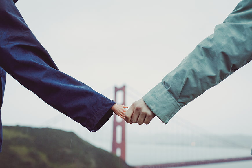 Couple holding hands with Golden Gate Bridge in foggy background