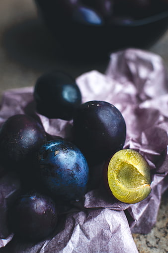 Fresh dark plums on crumpled paper with one cut open