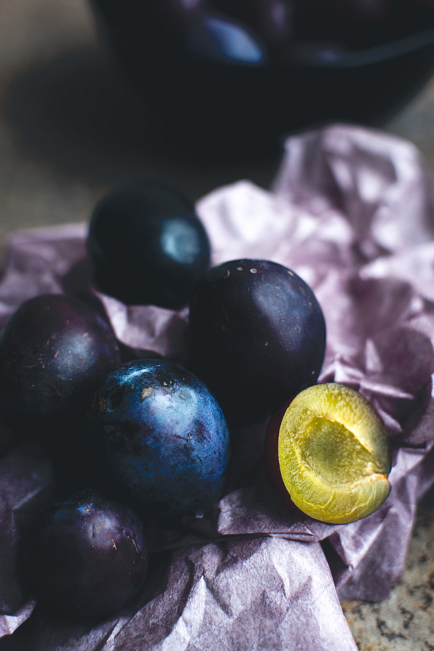 Fresh dark plums on crumpled paper with one cut open