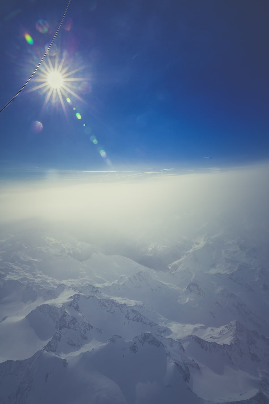 Aerial View of Snowy Mountain Peaks Above Clouds with Sun Flare