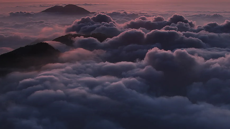 Sea of clouds over mountain peaks at sunset