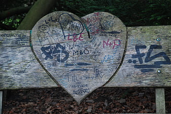 Graffiti covered wooden heart on park bench