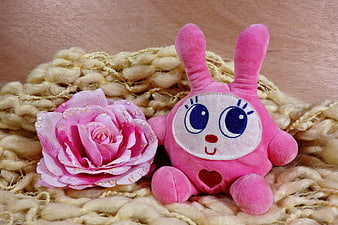 Pink plush rabbit toy with artificial rose on beige knitted blanket