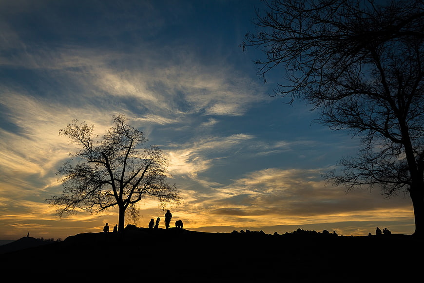 Silhouette of people and trees against a dramatic sunset sky
