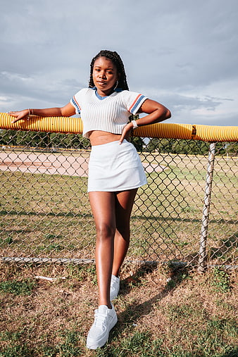 Stylish Black Woman in White Outfit Leaning on Fence
