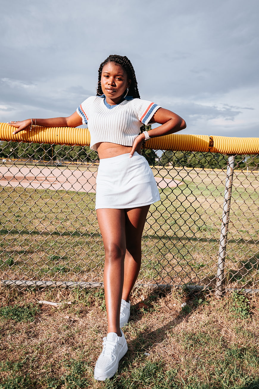 Stylish Black Woman in White Outfit Leaning on Fence