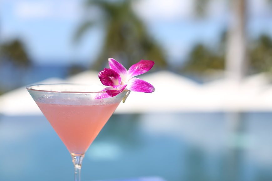 Pink cocktail with orchid garnish by tropical pool