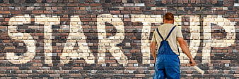 Painter writing startup on brick wall with stencil
