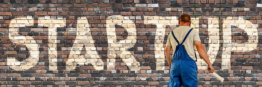 Painter writing startup on brick wall with stencil