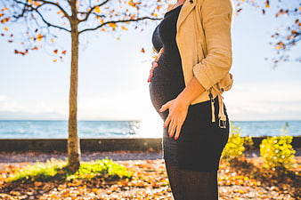 Pregnant woman holding belly in autumn park by sea