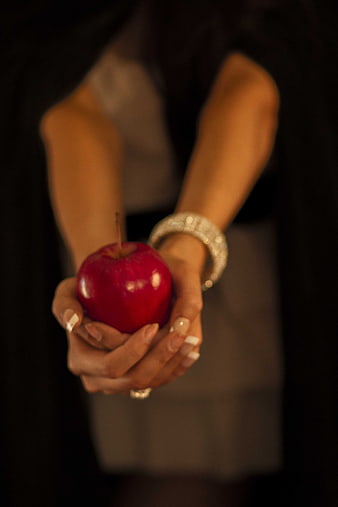 Woman holding a red apple with jewelry in dark setting