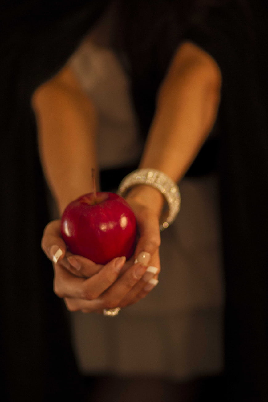 Woman holding a red apple with jewelry in dark setting